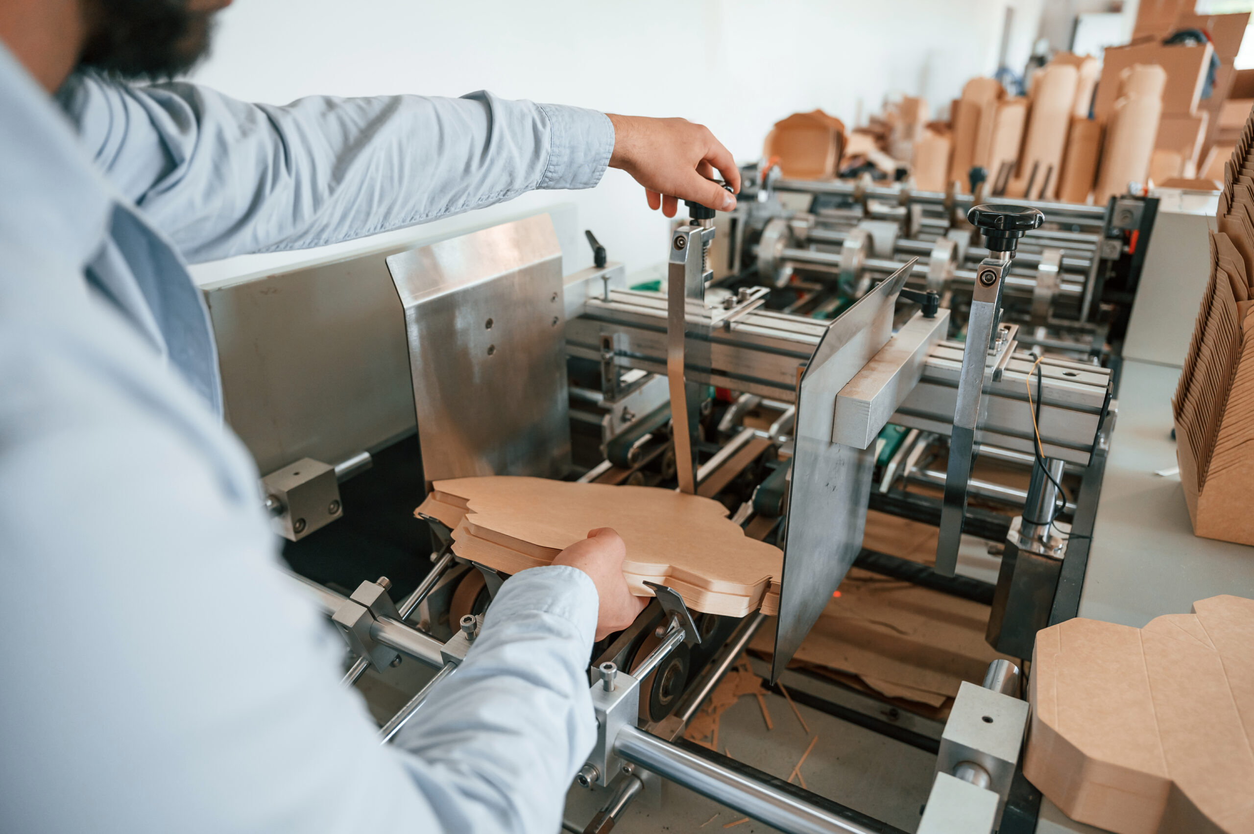 Operating printing cutting machine. Print house worker in white clothes is indoors.